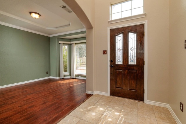 foyer featuring arched walkways, visible vents, baseboards, and a tray ceiling