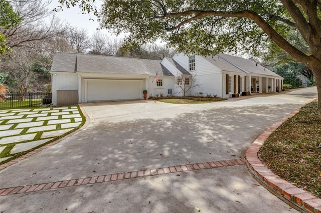 view of front of property featuring a garage, brick siding, driveway, and fence