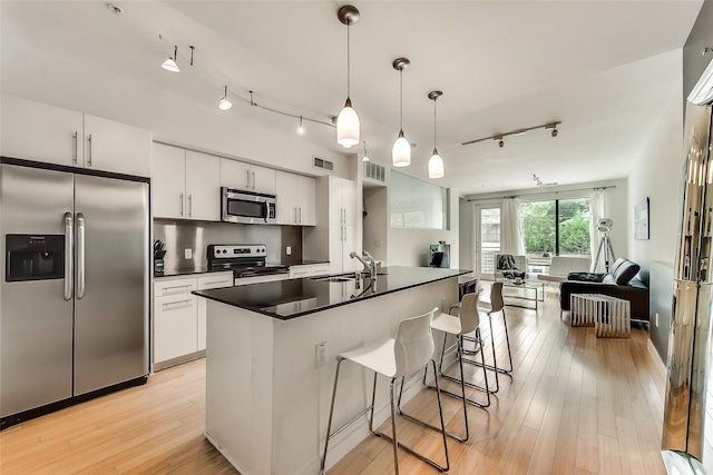 kitchen with dark countertops, light wood finished floors, open floor plan, stainless steel appliances, and a sink