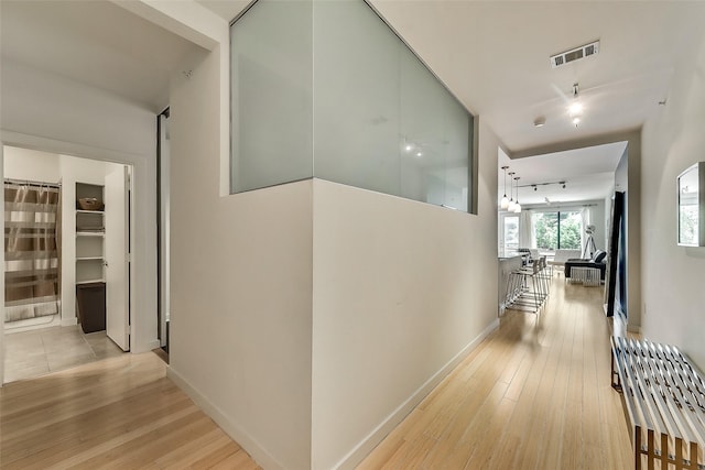 hallway featuring visible vents, baseboards, light wood-style flooring, and track lighting