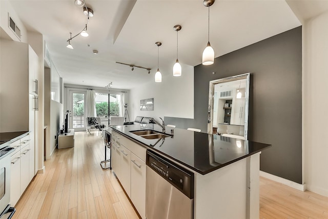 kitchen featuring a center island with sink, light wood finished floors, a sink, dishwasher, and dark countertops