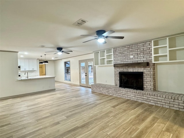 unfurnished living room featuring visible vents, light wood-style flooring, a fireplace, french doors, and a sink