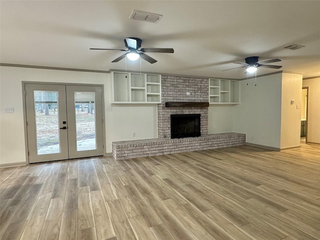 unfurnished living room with visible vents, light wood-style flooring, french doors, a fireplace, and crown molding