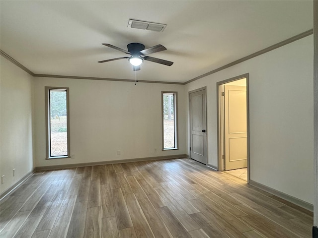 empty room featuring a ceiling fan, wood finished floors, visible vents, baseboards, and crown molding