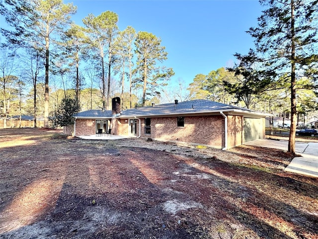 back of house featuring brick siding, driveway, a chimney, and a garage