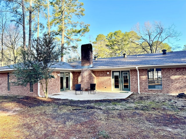 rear view of property with a patio area, french doors, brick siding, and a chimney