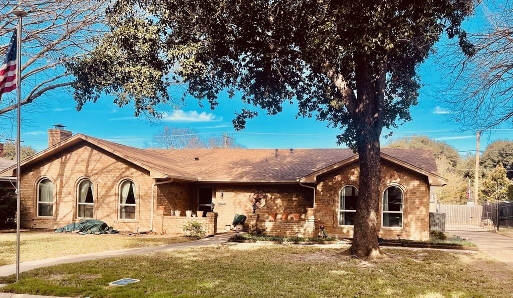 ranch-style house featuring brick siding, a chimney, a front lawn, and fence