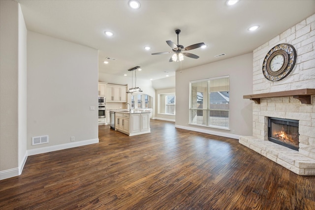 unfurnished living room with visible vents, a sink, dark wood finished floors, a stone fireplace, and ceiling fan