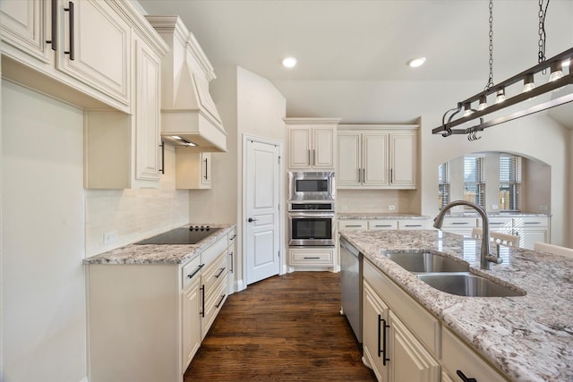 kitchen featuring dark wood-type flooring, light stone counters, custom exhaust hood, stainless steel appliances, and a sink