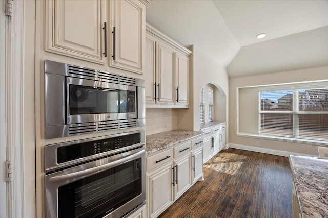 kitchen featuring light stone counters, baseboards, dark wood finished floors, vaulted ceiling, and appliances with stainless steel finishes