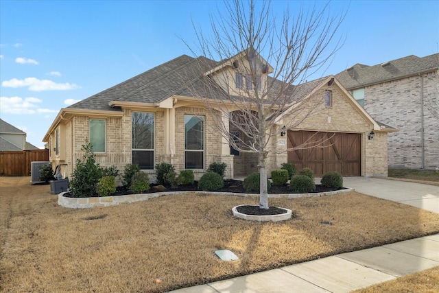 view of front facade featuring driveway, fence, a shingled roof, a garage, and brick siding