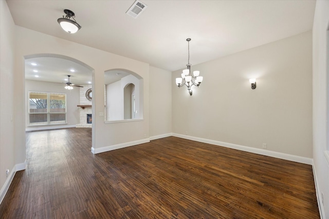 spare room with visible vents, baseboards, dark wood finished floors, ceiling fan with notable chandelier, and a fireplace