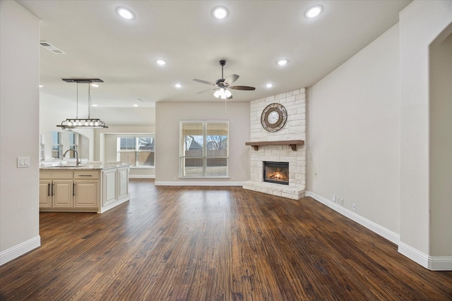 unfurnished living room featuring dark wood-type flooring, a fireplace, baseboards, and a sink