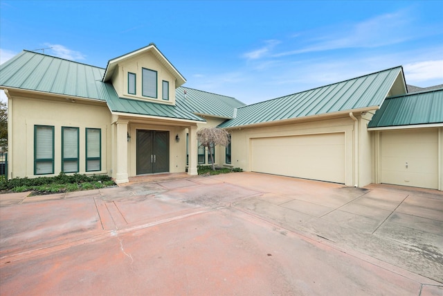 modern farmhouse with stucco siding, driveway, an attached garage, and a standing seam roof