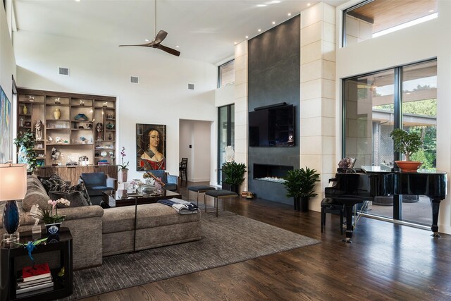 living room with a large fireplace, a ceiling fan, wood finished floors, and a towering ceiling