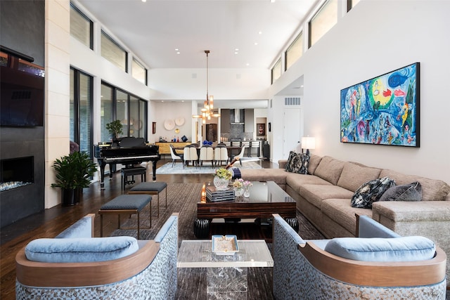 living room featuring visible vents, a chandelier, a fireplace, a towering ceiling, and wood finished floors