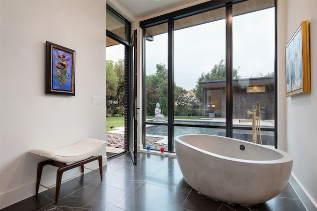 full bathroom with a wall of windows, a freestanding tub, baseboards, and tile patterned floors