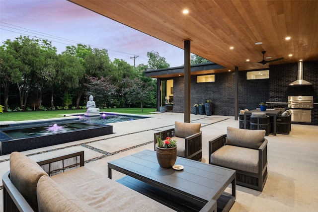 patio terrace at dusk featuring area for grilling, exterior kitchen, outdoor lounge area, an in ground hot tub, and ceiling fan