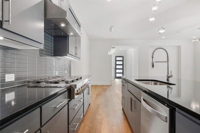 kitchen with a sink, tasteful backsplash, range hood, stainless steel appliances, and light wood finished floors