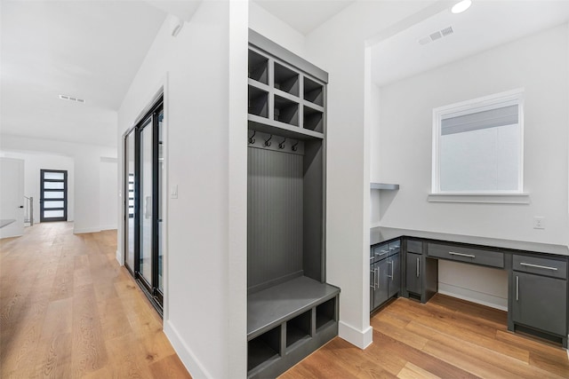 mudroom with light wood-style floors, visible vents, built in desk, and baseboards