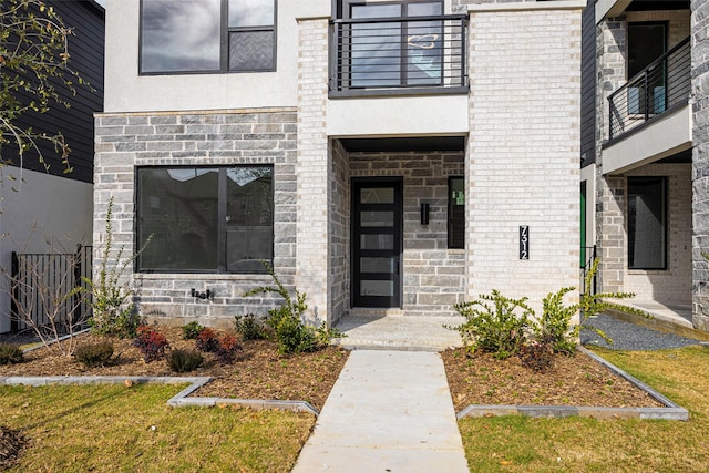 property entrance featuring stucco siding, stone siding, brick siding, and a balcony