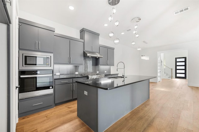 kitchen featuring gray cabinetry, a sink, under cabinet range hood, dark countertops, and appliances with stainless steel finishes