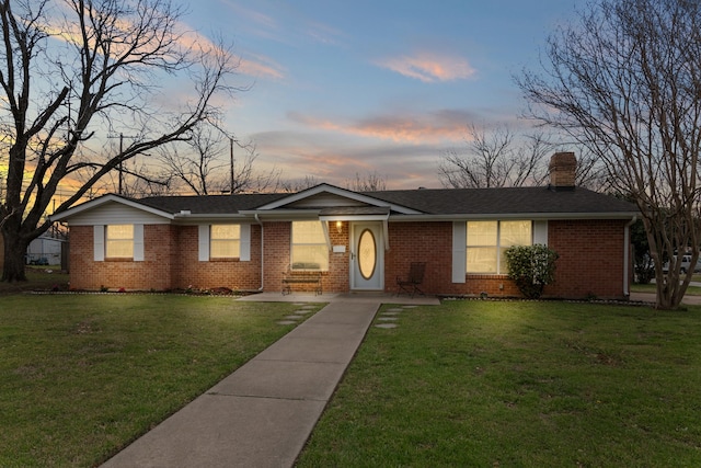 single story home with brick siding, roof with shingles, a chimney, and a lawn