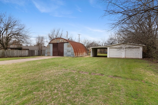 view of yard featuring a detached garage, an outbuilding, driveway, and fence