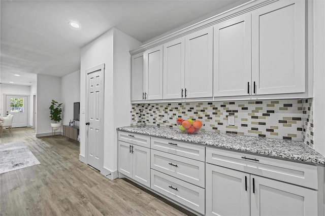 kitchen with decorative backsplash, light wood-style flooring, baseboards, and light stone countertops