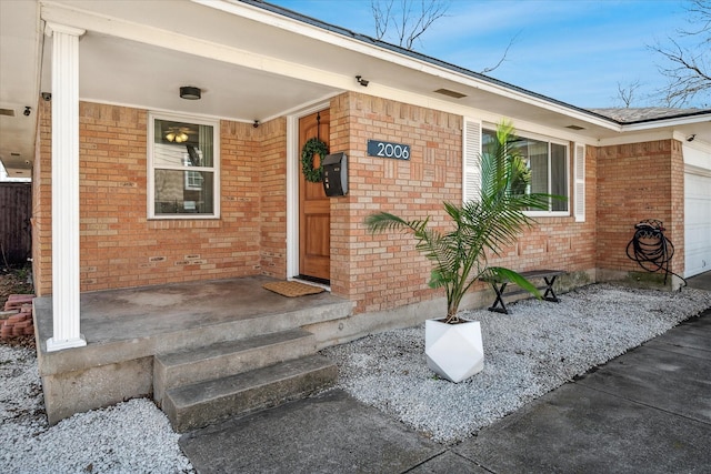 view of exterior entry featuring brick siding, a porch, and an attached garage