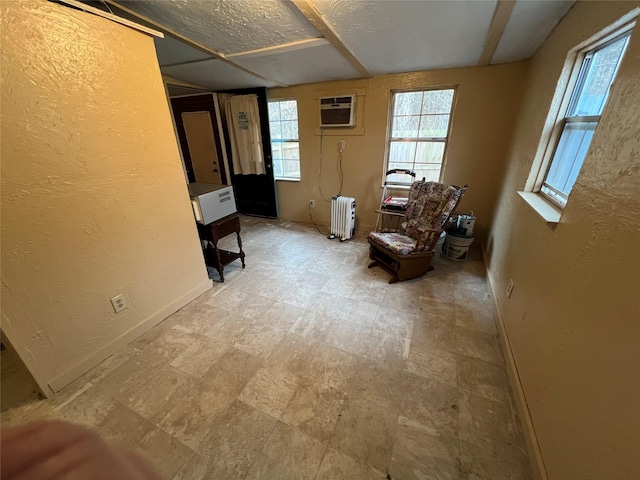 sitting room with radiator, a textured wall, baseboards, and a wall mounted AC