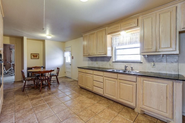 kitchen with dark countertops, light brown cabinets, backsplash, and a sink