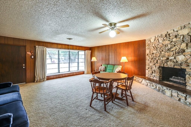 carpeted dining area featuring a stone fireplace, a textured ceiling, wood walls, and ceiling fan