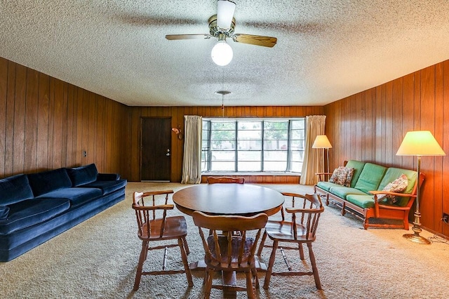 carpeted dining space with a textured ceiling, ceiling fan, and wood walls