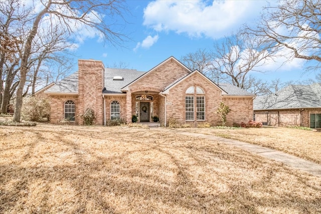 view of front of home with a front lawn, brick siding, and a chimney