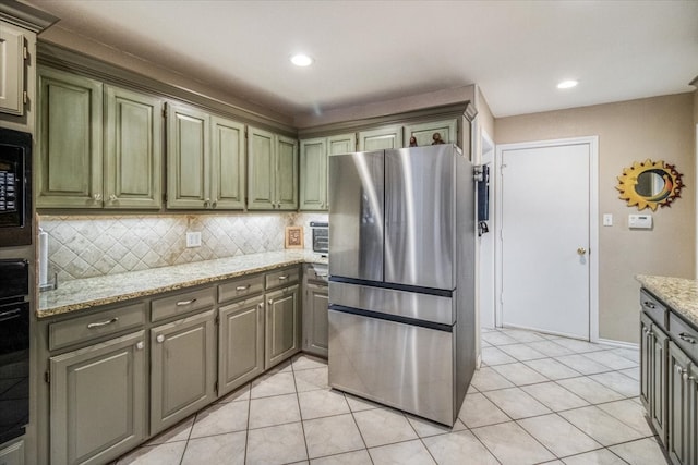 kitchen with light stone counters, freestanding refrigerator, green cabinetry, decorative backsplash, and light tile patterned floors