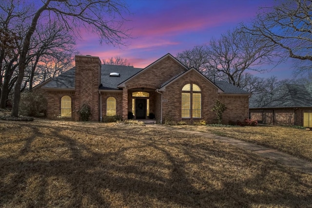 french provincial home with a front yard, brick siding, roof with shingles, and a chimney