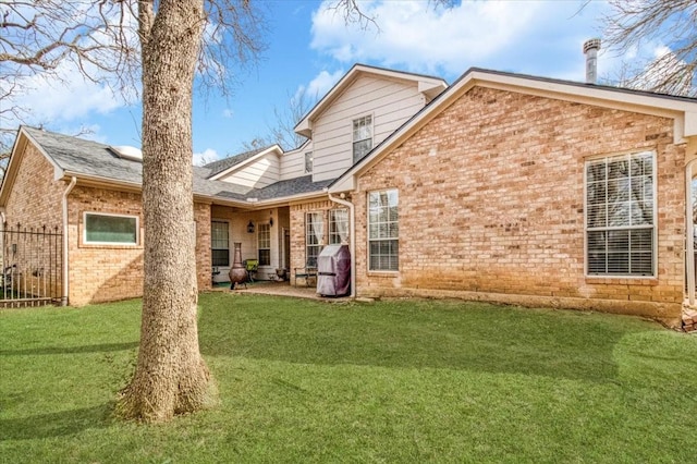 rear view of property featuring a lawn, brick siding, and a patio