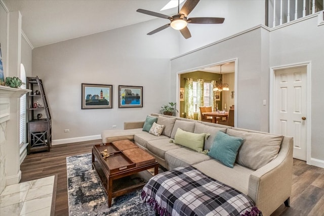 living area with high vaulted ceiling, ceiling fan with notable chandelier, dark wood-style floors, a premium fireplace, and baseboards