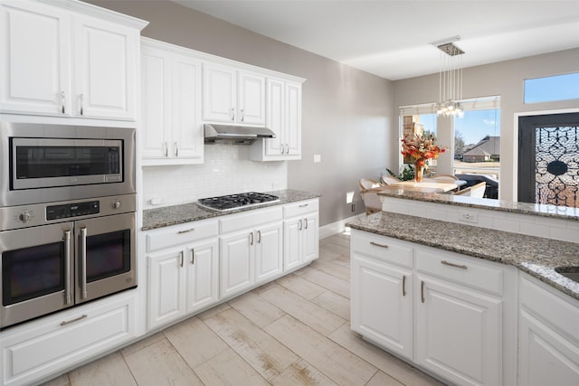 kitchen featuring under cabinet range hood, decorative backsplash, appliances with stainless steel finishes, and light stone countertops