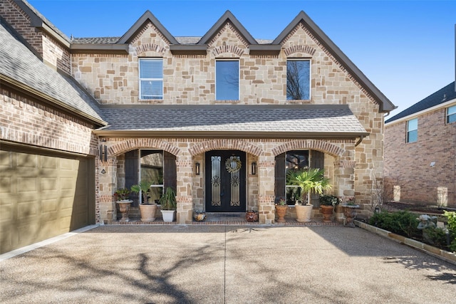 property entrance featuring french doors, stone siding, and roof with shingles