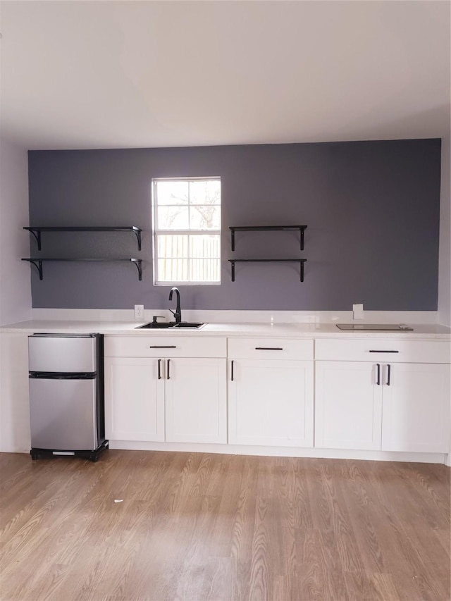 kitchen with a sink, open shelves, white cabinets, and freestanding refrigerator