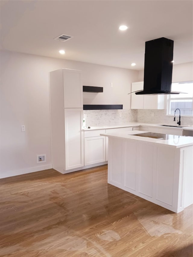 kitchen featuring light wood finished floors, visible vents, light countertops, island range hood, and white cabinetry