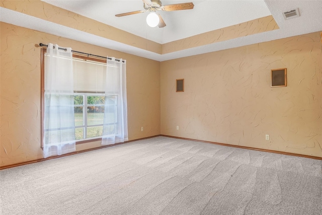 carpeted empty room featuring visible vents, a raised ceiling, baseboards, and a textured wall