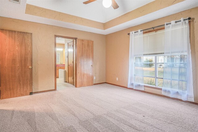 spare room featuring visible vents, a tray ceiling, baseboards, light colored carpet, and a textured wall