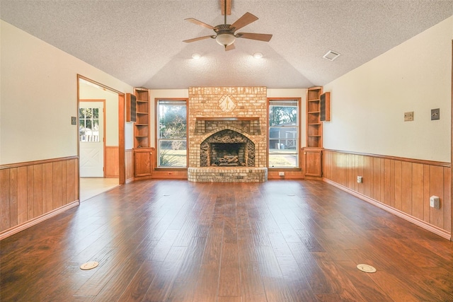 unfurnished living room with built in shelves, a healthy amount of sunlight, a wainscoted wall, and a textured ceiling