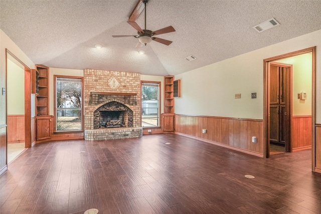 unfurnished living room featuring a textured ceiling, built in shelves, visible vents, and wainscoting