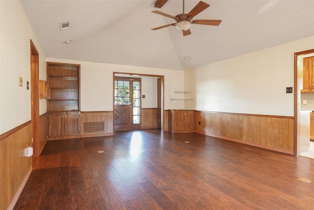 unfurnished room with lofted ceiling, visible vents, a wainscoted wall, and wood walls