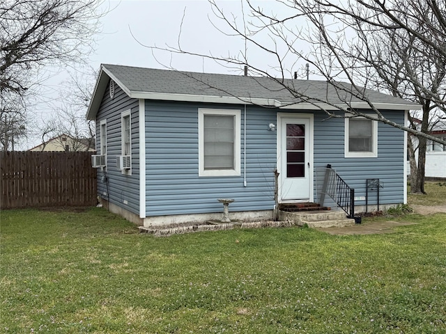 bungalow-style house featuring entry steps, a shingled roof, a front lawn, and fence