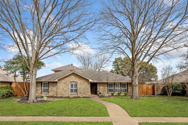 view of front of home featuring a front lawn, fence, brick siding, and a shingled roof